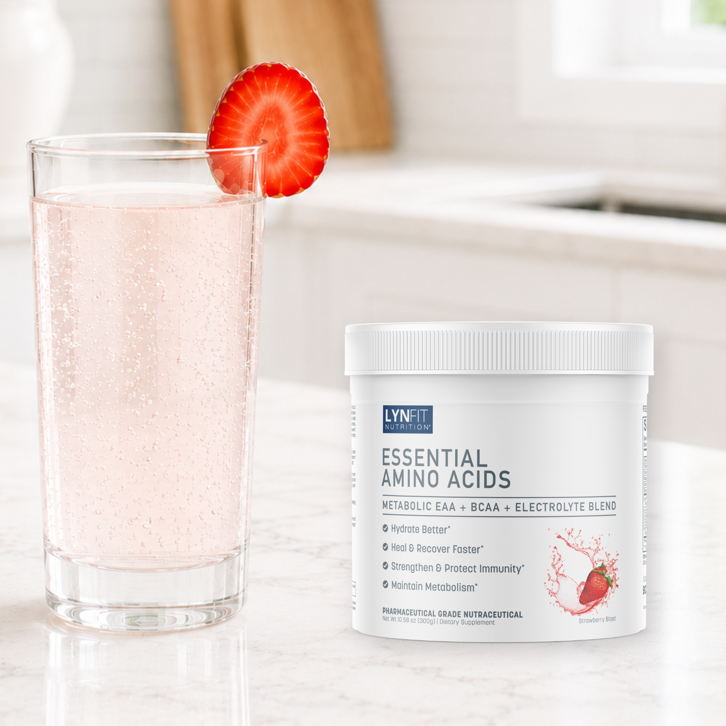 A white tub of LynFit Essentials Essential Amino Acids powder sits on a light marble countertop next to a glass of bubbly pink drink with a sliced strawberry garnish, set against a softly blurred kitchen background.