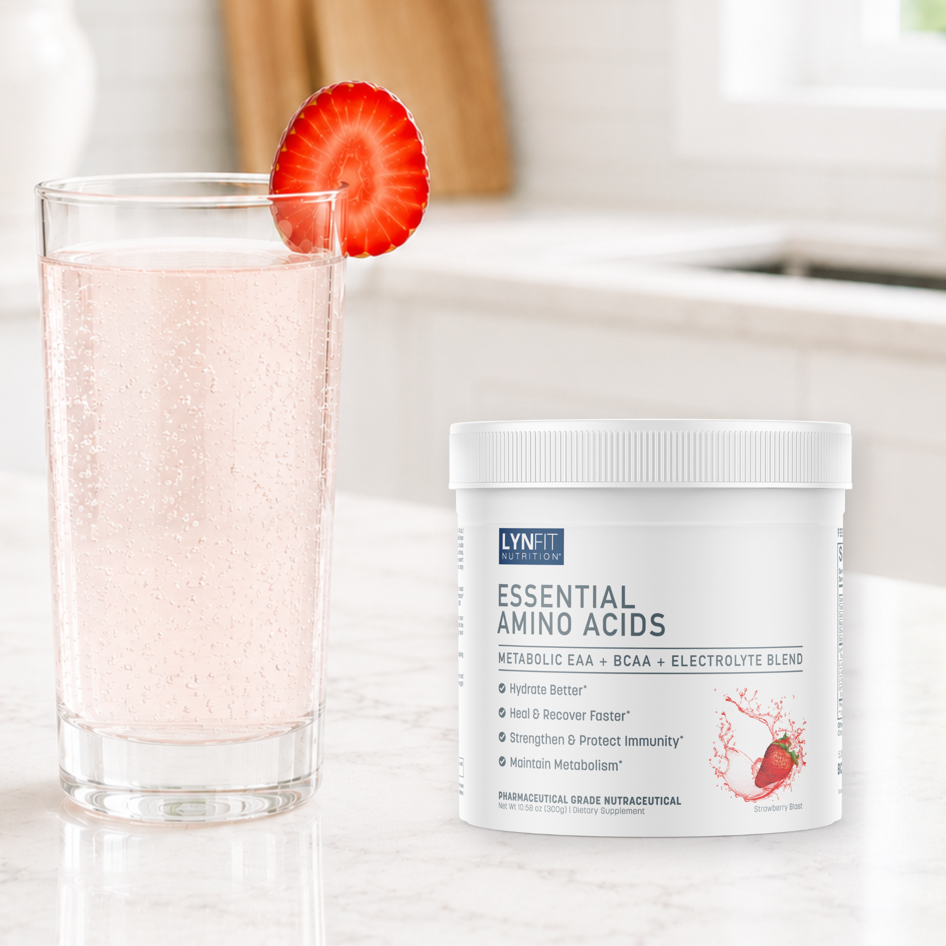 A white tub of LynFit Essentials Essential Amino Acids powder sits on a light marble countertop next to a glass of bubbly pink drink with a sliced strawberry garnish, set against a softly blurred kitchen background.